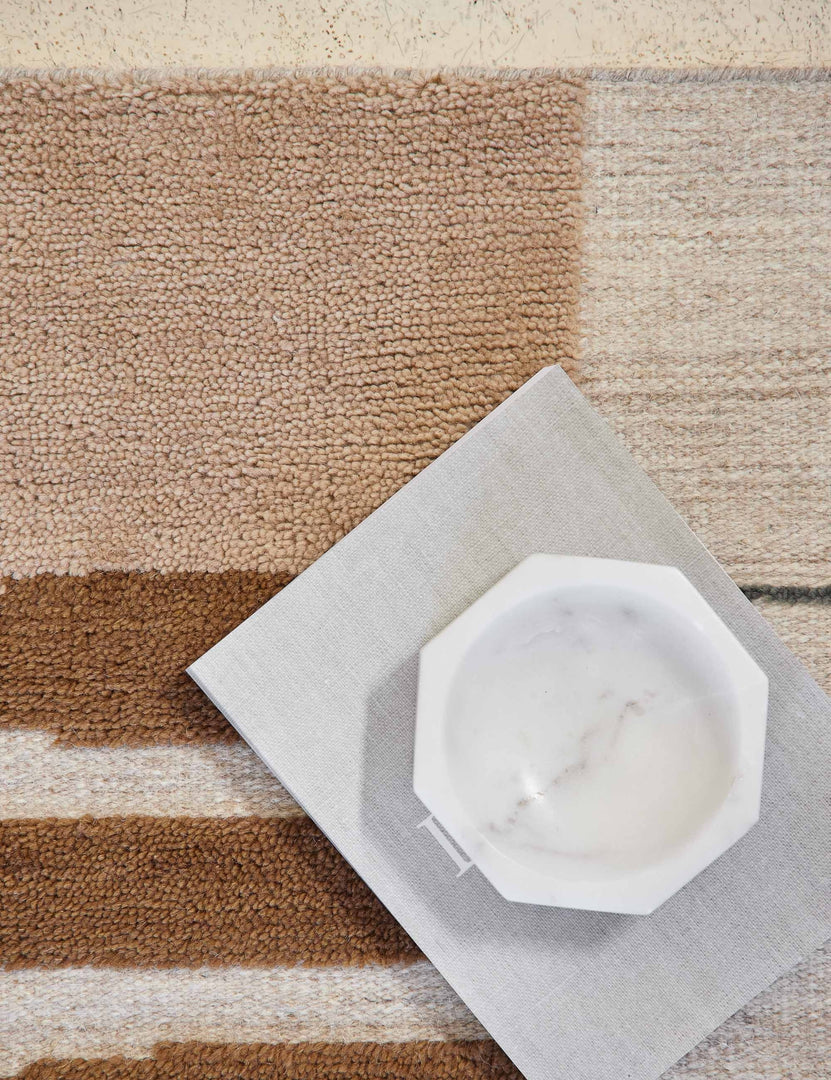 #size::2--x-3- #size::2-6--x-8- #size::5--x-8- #size::6--x-9- #size::8--x-10- #size::9--x-12- #size::10--x-14- #size::12--x-15- | Close-up of the Benita natural toned hand-knotted floor rug by Nina Freudenberger with a book and marble octagonal bowl sitting atop it