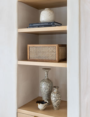 Rattan cane bin by NEAT Method sits on a shelf with a book and various vases