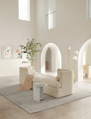 The gray dylan rug lays in a room with high ceilings under a narrow cream media lounger and a sculptural stone side table