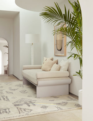 The Nabu white metal floor lamp with ribbed base and gold accents by Regina Andrew sits in the corner of an entry way with a plush geometric rug, a beige linen sofa, and a natural toned wall art