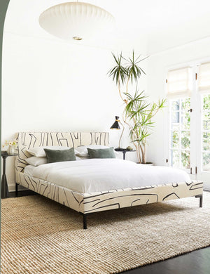 The Deva Grafitto platform bed lays in a bright bedroom in between two round side tables and atop a jute rug