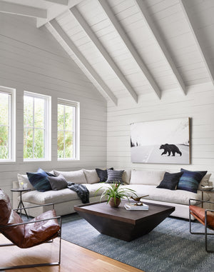 The Alison geometric square coffee table sits in a living room with a sloped ceiling, a linen sectional sofa, and two brown leather accent chairs