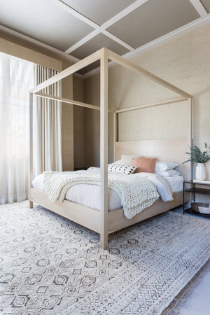 The Sable white swan ultra-chunky throw blanket by Nikki Chu lays in a bedroom at the edge of a white-washed wooden canopy bed that sits atop a textured white and brown carpet