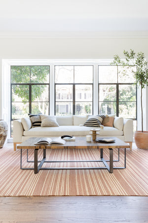 The Charleston Ivory Linen sofa sits against a bright window atop an ochre and white striped carpet