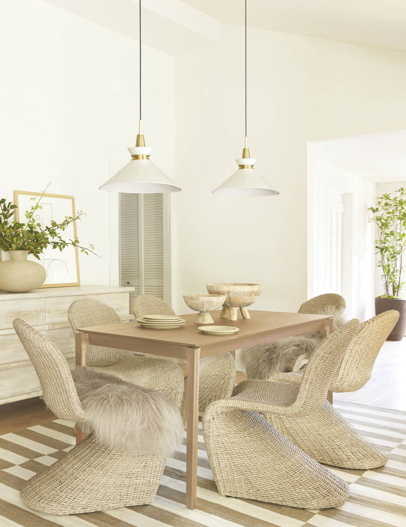 #size::large #color::gold #size::small | The Kloe conical Pendant Light with a white finish and aged brass hardware is mounted in a dining room with neutral woven dining chairs, a light wooden dining table, and a white and brown striped rug