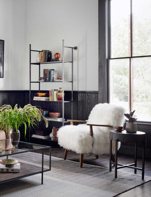 The Kora accent chair sits in a living room with black paneled walls, a gray-toned rug, and a black side table