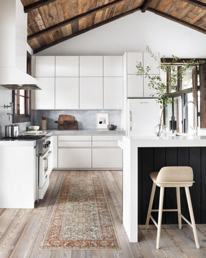 The Daelon persian and vintage inspired rug in its runner size lays in a kitchen with white cabinetry and a wooden bar stool atop hardwood floors