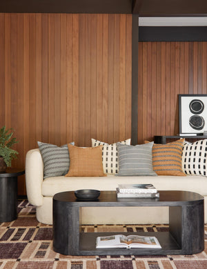 Bertu pumice gray pillow with a woven dash pattern by Bolé Road Textiles sits on a cream boucle rounded sofa in a retro living room