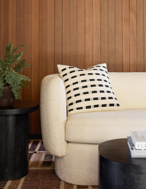 Bertu onyx black pillow with a woven dash pattern by Bolé Road Textiles sits on a cream boucle rounded sofa in a room with wooden paneled walls