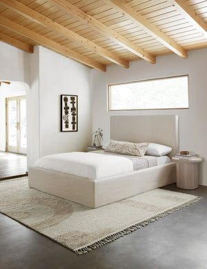 The Nomad neutral-toned geometric floor rug with subtle ribbed design by Élan Byrd lays in a bedroom with a geometric black and white wall art, a natural linen framed queen bed, and white-washed wooden nightstands