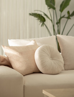 The Monroe oyster white velvet round pillow sits on a white accent chair
