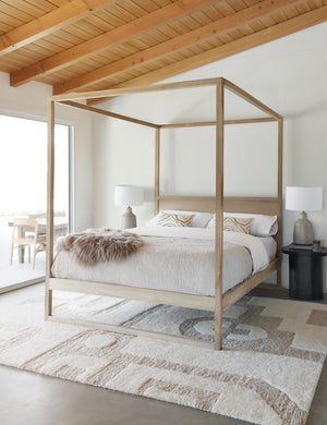 Canyon Terracotta Lumbar Pillow sits on a wooden canopy bed in a room with a cream and neutral geometric rug and a wooden ceiling