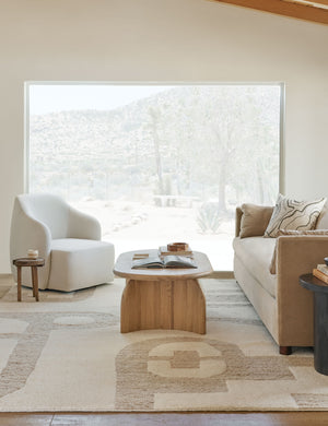  The Tobi natural linen swivel chair sits atop a natural and ivory patterned carpet in front of a large window with a desert view