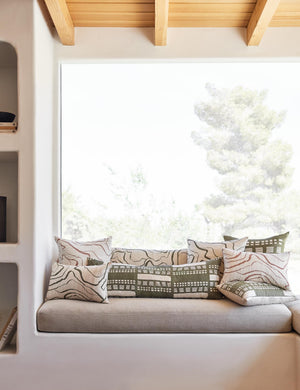 Canyon Olive Green Long Lumbar Pillow sits on a bench with other canyon throw pillows in front of a large window