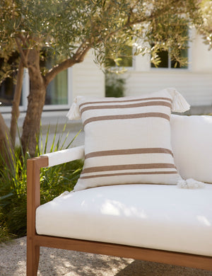 The Fez camel and white indoor and outdoor throw pillow sits on a white sofa in an outdoor space