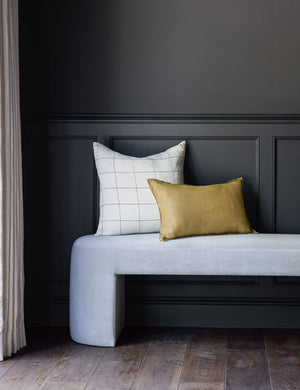 The lucian white and black square pillow sits with a yellow pillow on a light blue velvet bench against a black wall
