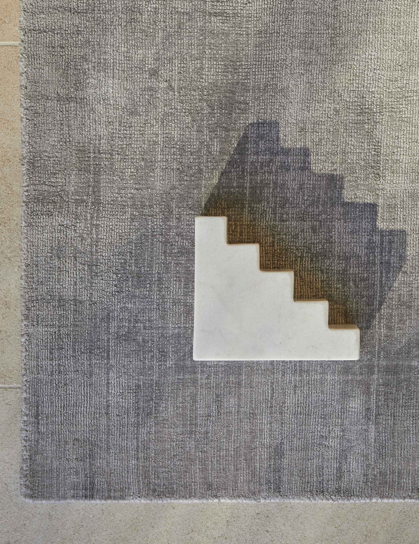 #color::gray #size::6--x-9- #size::8--x-10- #size::9--x-12- #size::10--x-14- #size::12--x-15- | Bird's-eye view of the corner of the gray dylan rug with a staircase shaped white sculptural object sitting atop it