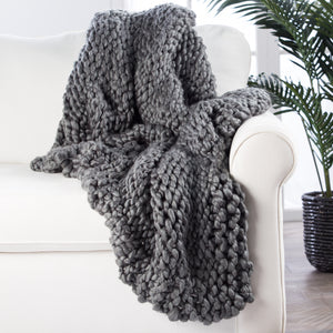 The Sable flint gray ultra-chunky throw blanket by Nikki Chu lays atop a white linen sofa