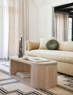 The Monroe moss green velvet round pillow sits on a natural sofa in a living room with an oval coffee table and geometric rug