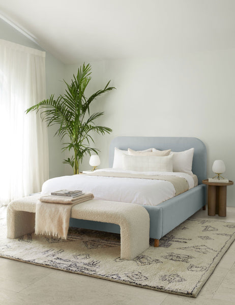 #showall::39616857374819 | The Solene dove light blue velvet platform bed sits atop a plush patterned rug with a boucle cream bench and white linens