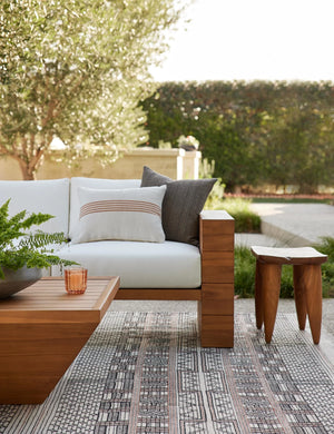 Katya Indoor and Outdoor lumbar cream Pillow with rust brown stripes in the center sits on a white cushioned coach outside next to a gray pillow