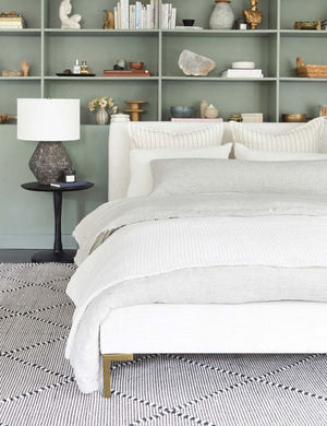  The Deva Talc Linen platform bed lays in a bedroom with a green inset shelf atop a black and white rug