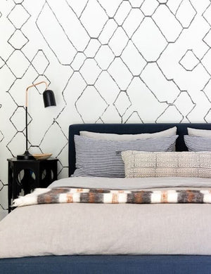 The Set of two european flax linen indigo blue striped pillowcases by cultiver lay on a blue velvet framed bed in a bedroom with white and black patterned walls and a black hexagonal nightstand